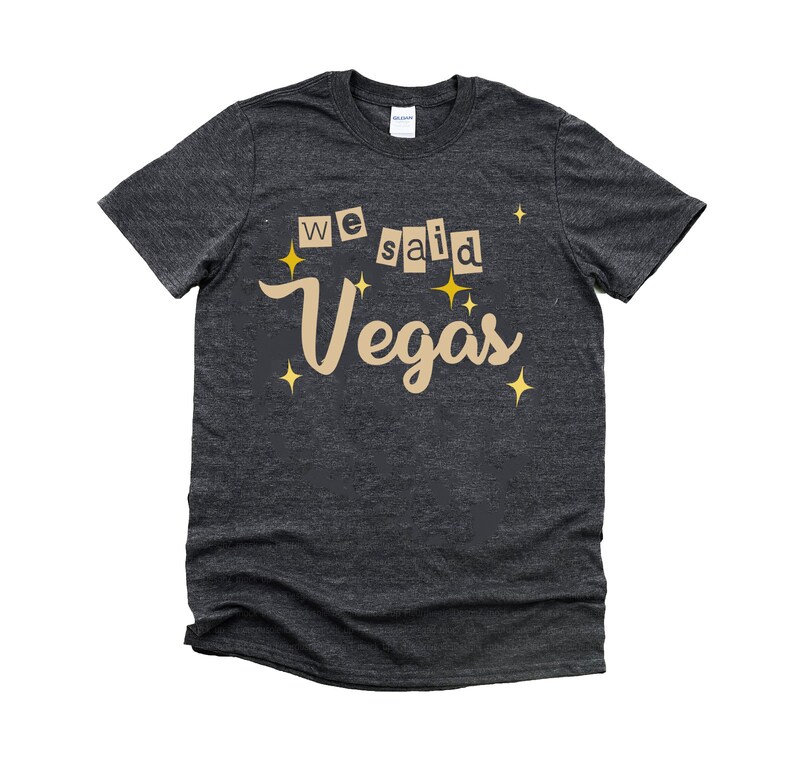 May include: A dark heather grey t-shirt with the text "We said Vegas" in a tan color with gold stars.