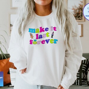 May include: White sweatshirt with the text "make it last forever" in rainbow colors. The text is surrounded by small cartoon images of a troll doll, a diamond ring, and a lava lamp.