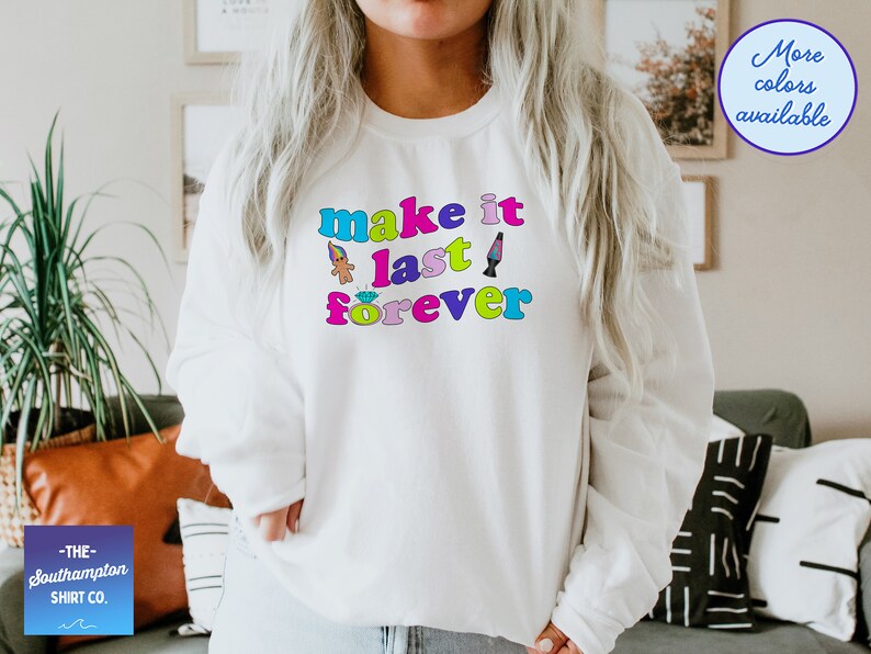 May include: White sweatshirt with the text "make it last forever" in rainbow colors. The text is surrounded by small cartoon images of a troll doll, a diamond ring, and a lava lamp.