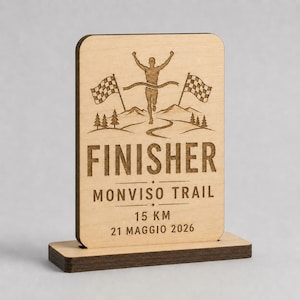 Peut inclure: Plaque en bois clair avec un coureur franchissant la ligne d'arrivée, des drapeaux à damiers et le mot "FINISHER". Le texte "MONVISO TRAIL", "15 KM" et "21 MAGGIO 2026" sont gravés. La plaque est sur un socle marron foncé. 15 kilomètres.
