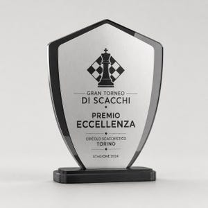 Può includere: Una targa premio a forma di scudo con una superficie in metallo argento spazzolato e un bordo nero, montata su una base rettangolare nera. La targa presenta un'icona nera di un re degli scacchi sopra il testo GRAN TORNEO DI SCACCHI, PREMIO ECCELLENZA, CIRCOLO SCACCHISTICO TORINO e STAGIONE 2024.