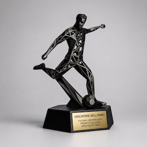 Peut inclure: Une sculpture géométrique noire représentant un joueur de football en train de frapper un ballon. La figurine est faite de formes triangulaires interconnectées. La sculpture repose sur une base noire avec une plaque dorée indiquant "GIOCATORE DELL'ANNO".