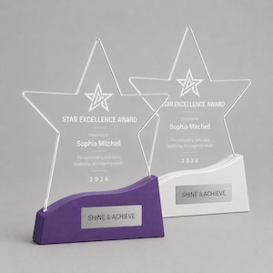 Peut inclure: Deux trophées en forme d'étoile avec des faces en acrylique transparentes et des socles colorés. L'un a une base violette, l'autre blanche. Le texte sur les récompenses indique "STAR EXCELLENCE AWARD", "Présenté à Sophia Mitchell" et "SHINE & ACHIEVE".
