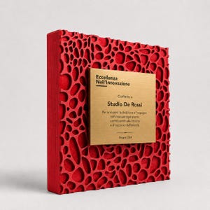 Può includere: Un premio rosso con superficie strutturata e placca dorata. La placca recita "Eccellenza Nell'Innovazione" e "Studio De Rossi". Il premio è datato giugno 2024. Il premio presenta un motivo organico unico.