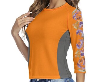 May include: An orange three-quarter sleeve top with a gray side panel and floral design on the right sleeve. The top is paired with blue jeans. The floral design features orange, purple, and yellow flowers.