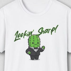 Peut inclure: T-shirt blanc avec un cactus de dessin animé en smoking et le texte "Lookin' Sharp!" en vert. Le cactus souriant porte un smoking noir avec un nœud papillon. Un design amusant et ludique.