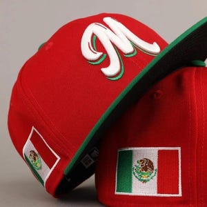May include: Red baseball cap with a green brim and the letter "M" in white with green trim. The cap features the Mexican flag on the side. The cap is a fitted style.