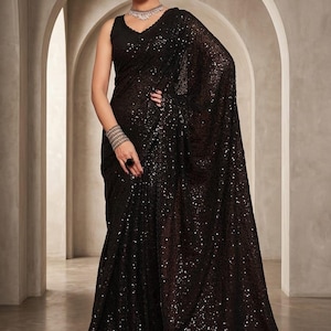 May include: A sleeveless black saree featuring an all-over sequin embellishment that creates a shimmering effect. The garment is draped in a traditional style with a matching black blouse, paired with a silver-toned necklace and a wide bracelet.