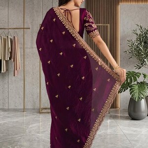 Peut inclure: Un sari violet fonc&eacute; avec broderie dor&eacute;e. Le sari pr&eacute;sente des d&eacute;tails dor&eacute;s complexes le long de la bordure et dispers&eacute;s sur le tissu. Les manches du chemisier sont &eacute;galement orn&eacute;es de broderies dor&eacute;es. Le sari est drap&eacute; sur une personne.