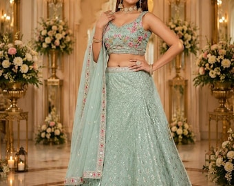 Op de afbeelding: Een mintgroene lehenga-set bestaande uit een mouwloze top en een rok tot op de grond, beide versierd met bloemenborduursels in roze en groene tinten, zilveren lovertjes en een bijpassende transparante dupatta met een decoratieve rand.