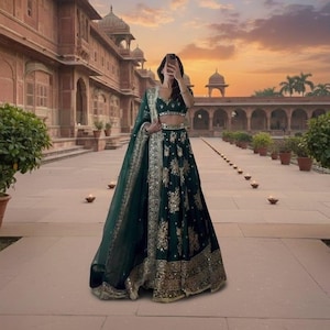 Może przedstawiać: Ciemnozielona lehenga ze złotym haftem. Str&oacute;j zawiera pasujący dupatta i kr&oacute;tki top. Lehenga ma skomplikowane złote detale wzdłuż obszycia i obramowań. Tło przedstawia zach&oacute;d słońca i budynek z łukami.