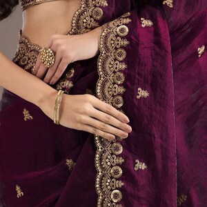Peut inclure: Un sari violet profond avec des broderies dor&eacute;es complexes et des d&eacute;tails de sequins. Le sari pr&eacute;sente une bordure d&eacute;corative et de petits ornements dor&eacute;s dispers&eacute;s. Un chemisier assorti avec broderie dor&eacute;e est &eacute;galement visible.