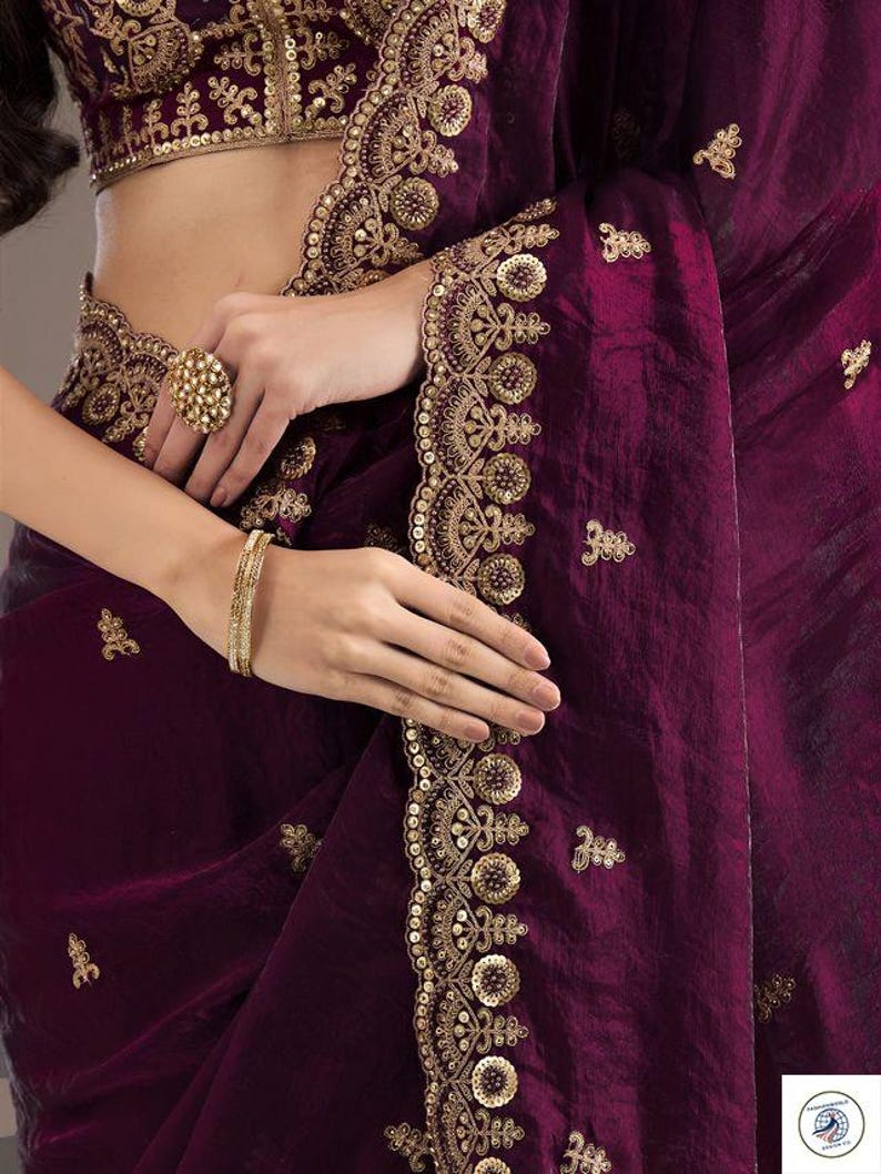 Peut inclure: Un sari violet profond avec des broderies dor&eacute;es complexes et des d&eacute;tails de sequins. Le sari pr&eacute;sente une bordure d&eacute;corative et de petits ornements dor&eacute;s dispers&eacute;s. Un chemisier assorti avec broderie dor&eacute;e est &eacute;galement visible.
