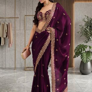 Peut inclure: Un sari violet fonc&eacute; avec des broderies dor&eacute;es complexes sur les bordures et le corsage. Le sari comprend un chemisier assorti avec des ornements dor&eacute;s d&eacute;taill&eacute;s. Une petite pochette rose compl&egrave;te l'ensemble. Le style g&eacute;n&eacute;ral est &eacute;l&eacute;gant et formel.