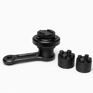 Op de afbeelding: Zwarte telefoonhouder voor motorfietsen met een draaiarm en twee cilindrische montagecomponenten. De houder heeft een cirkelvormige basis en een gestructureerd oppervlak. De componenten zijn ontworpen om een telefoon veilig vast te houden tijdens het rijden.