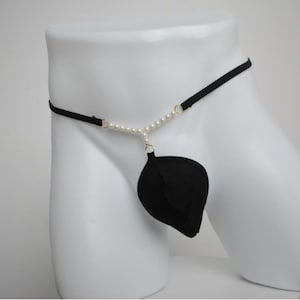 Könnte beinhalten: Schwarzer String-Tanga mit einem blattförmigen Beutel. Der String hat einen schwarzen elastischen Bund und eine Perlenkette. Die Perlen sind mit einem goldfarbenen Ring mit dem Beutel verbunden.