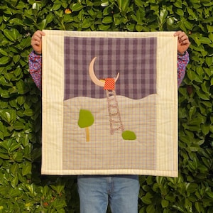 Può includere: Una trapunta fatta a mano con una scena notturna stravagante. La trapunta presenta una luna crescente, una scala e un albero, il tutto su uno sfondo a scacchi e a righe. La tavolozza dei colori include sfumature di viola, giallo e verde.