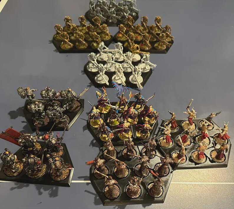 Puede incluir: Una colecci&oacute;n de figuras en miniatura, pintadas en varios colores, dispuestas en bandejas hexagonales negras. Las figuras representan personajes de fantas&iacute;a, incluyendo guerreros y criaturas, para juegos de mesa.