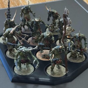 Puede incluir: Un conjunto de figuras de fantas&iacute;a en miniatura, pintadas en tonos verdes, marrones y beige. Las figuras est&aacute;n dispuestas en una bandeja negra con compartimentos circulares. Algunas figuras tienen cuernos, garras y armas. Para juegos de mesa.