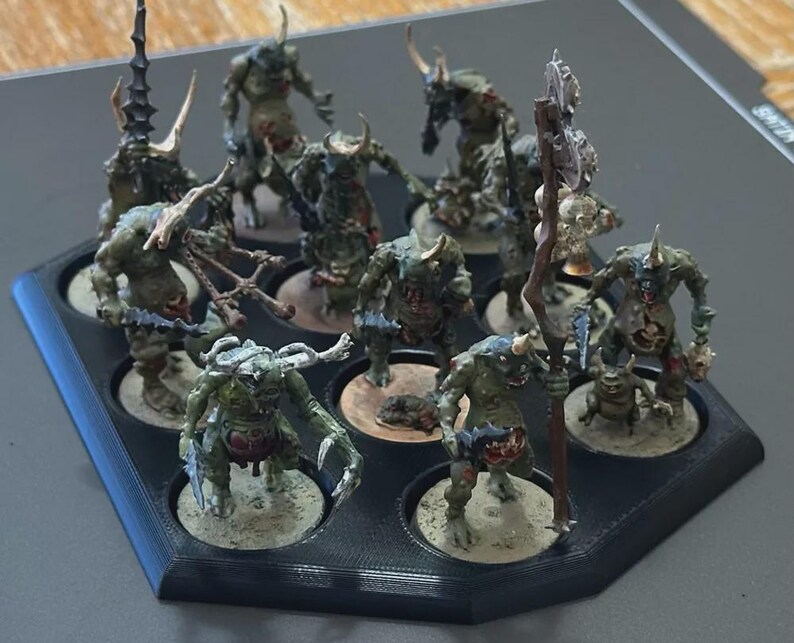 Puede incluir: Un conjunto de figuras de fantas&iacute;a en miniatura, pintadas en tonos verdes, marrones y beige. Las figuras est&aacute;n dispuestas en una bandeja negra con compartimentos circulares. Algunas figuras tienen cuernos, garras y armas. Para juegos de mesa.