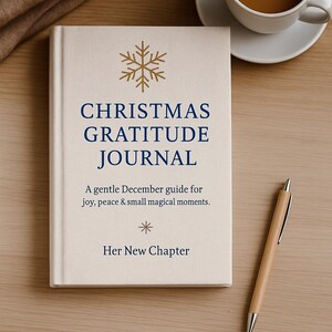 May include: A cream-coloured "Christmas Gratitude Journal" book with gold snowflake and text. A cup of coffee and a pen rest on a wooden surface. The journal's text reads: "A gentle December guide for joy, peace & small magical moments."