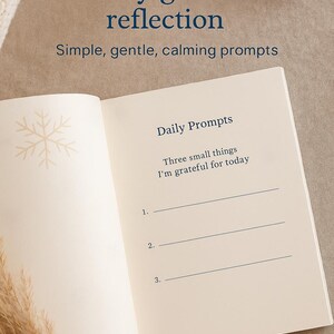 May include: An open journal with the text "Daily guided reflection" and "Daily Prompts". The journal prompts the user to list three things they are grateful for. A snowflake design is in the upper left corner.