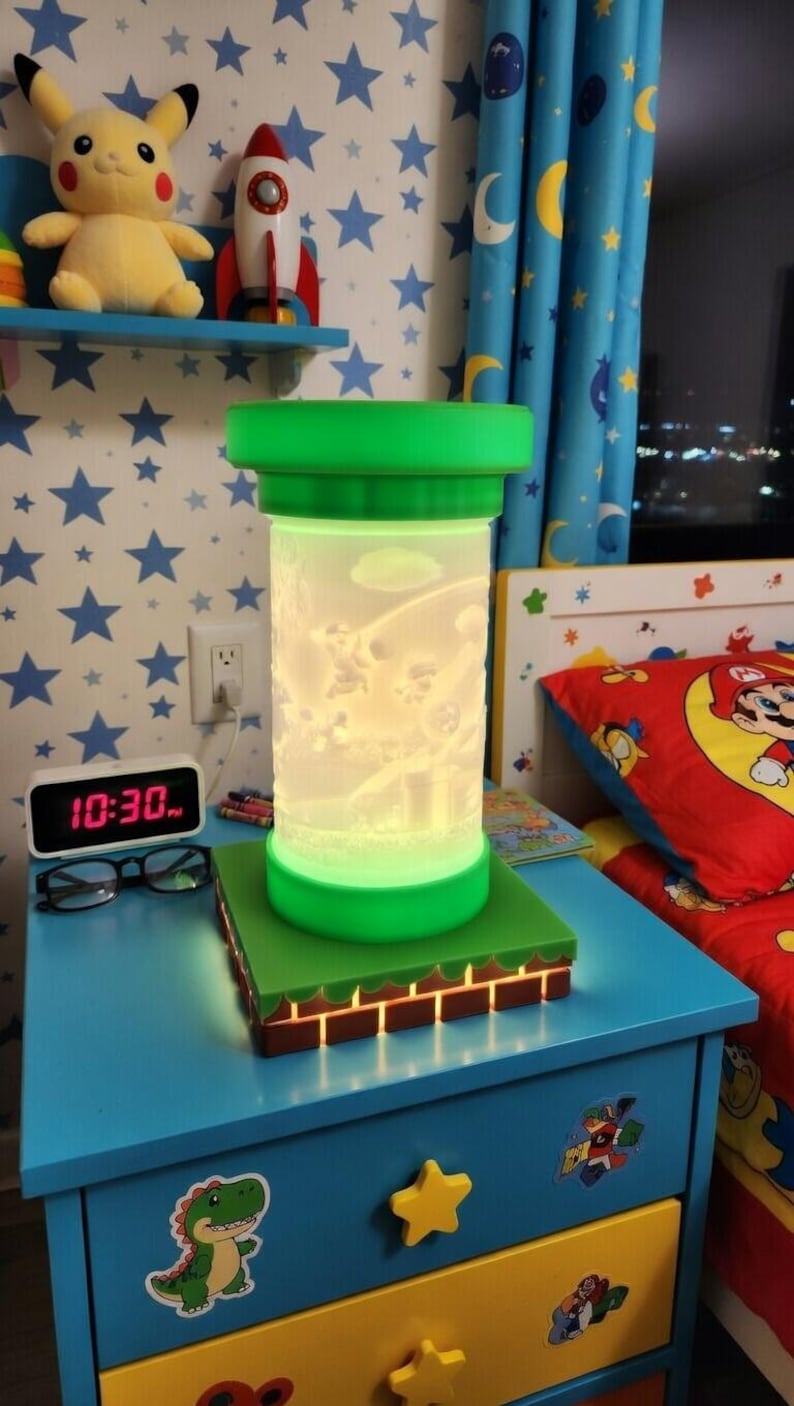 May include: A green and white cylindrical night light with a cartoon scene inside, sitting on a green and brown base. The lamp is on a blue nightstand with a dinosaur sticker. A Pikachu plush and a rocket are on a shelf above.