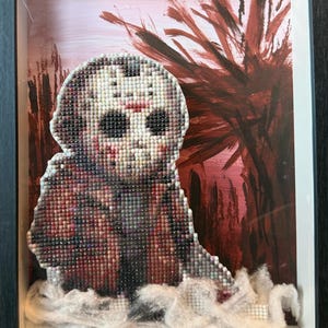 May include: Framed artwork featuring a mosaic of a masked figure, likely from a horror film, with a red and white color scheme. The mosaic is set against a backdrop of abstract red brushstrokes and white fluffy material.