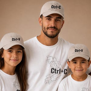 Puede incluir: Tres personas con atuendos a juego. Cada persona lleva una gorra de béisbol beige con "Ctrl+C" o "Ctrl+V" impreso en la parte delantera. También llevan camisetas blancas con un diseño de placa de circuito y "Ctrl+C" impreso en la parte delantera.