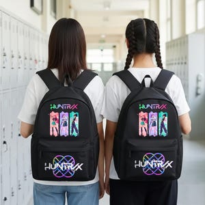 Może przedstawiać: Dwa czarne plecaki ze słowem "HUNTR/X" w kolorze białym i kolorową grafiką. Każdy plecak ma przednią kieszeń i wyściełane paski na ramiona. Plecaki są noszone przez dwie osoby.