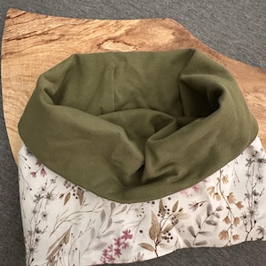 May include: A cowl neck scarf featuring a solid olive green fabric on the upper portion and a cream-colored fabric on the lower portion, which is decorated with a botanical print of small flowers, leaves, and branches in muted brown and pink tones.