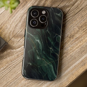 May include: A smartphone case with a dark green marble design. The case has a glossy finish and features a gold vein pattern. The phone case is on a wooden surface, with a camera and plant in the background.