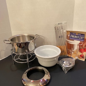 May include: A stainless steel fondue set including a metal pot on a stand, a white ceramic bowl, a chrome ring, and a pack of fondue forks with wooden handles. A product box with the text FONDUE SET STAINLESS STEEL is included.