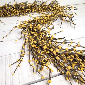 May include: A long garland of yellow berry stems with small green leaves. The garland is draped over a white wooden surface.