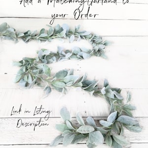 May include: A close-up of a garland of faux lambs ear leaves on a white wooden background. The text "Add a Matching Garland to your Order" is at the top of the image. The text "Link in Listing Description" is at the bottom of the image.