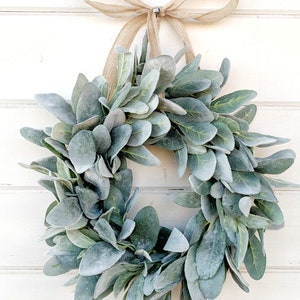 May include: A green and gray faux lamb's ear wreath with a burlap bow.