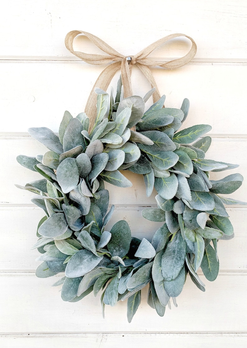May include: A green and gray faux lamb's ear wreath with a burlap bow.