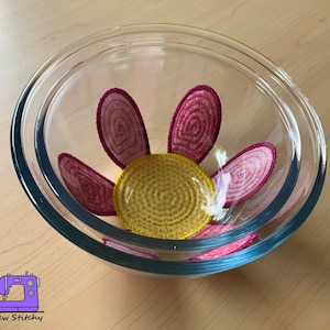 以下が含まれることがあります： 透明なガラスのボウルの中に、ピンクと黄色の花柄のデザインがあります。花は5枚の花びらと黄色の中心を持っています。