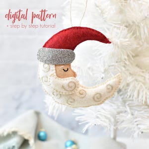 Puede incluir: Adorno navideño de fieltro con forma de media luna con gorro de Papá Noel. La luna es de color crema con detalles bordados, una cara bronceada y un gorro rojo con una banda de purpurina plateada. El texto "digital pattern + step by step tutorial" está en la parte superior.