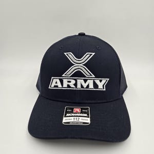 Puede incluir: Una gorra tipo camionero azul marino con parte trasera de malla y un logotipo X bordado en plata y blanco sobre la palabra ARMY en letras blancas. Una pegatina rectangular negra y blanca de Richardson 112 está en la visera curva.