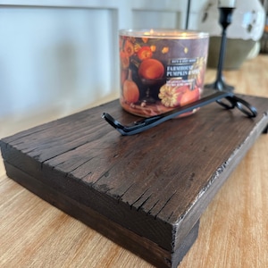 May include: A dark brown, rectangular wooden tray with a candle and wick trimmer. The candle has a label with the words "Farmhouse Pumpkin" and images of pumpkins. The wick trimmer is black and rests on the tray.