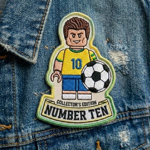 May include: An embroidered patch featuring a stylized minifigure character wearing a yellow jersey with the number 10 in blue, blue shorts, and holding a black and white soccer ball. The text reads COLLECTOR'S EDITION NUMBER TEN.