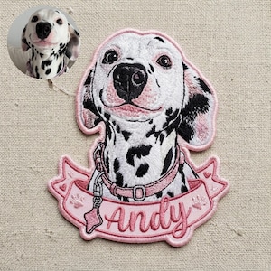 May include: An embroidered patch featuring a white Dalmatian dog with black spots, wearing a pink collar with a bone-shaped tag. Below the dog is a pink ribbon banner with the name Andy embroidered in script, accented by small paw prints.