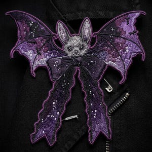 May include: An embroidered patch featuring a gray bat with large wings displaying a purple and black galaxy pattern with small white stars. A large, dark purple bow with a starry texture is positioned below the bat's head, with two long ribbons extending downward.
