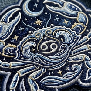 May include: A dark blue embroidered patch featuring a crab with intricate wave patterns on its shell and claws. The design includes a central Cancer zodiac symbol, a crescent moon, and scattered gold stars against a deep navy background.