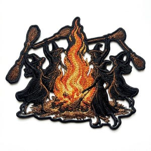 May include: An embroidered patch featuring five figures in black pointed hats and long dresses dancing around a central bonfire. The flames are rendered in shades of orange, yellow, and red. Two figures hold brown broomsticks above their heads.