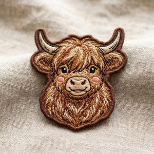 May include: An embroidered patch featuring the head of a Highland cow with long, shaggy brown fur, curved cream-colored horns, and small pink cheeks. The design is outlined in a dark brown border, showcasing detailed stitching and a friendly expression.