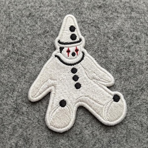 May include: An embroidered patch shaped like a white clown figure wearing a pointed hat. The figure features black circular buttons down the center, black circular accents on the hat and feet, and red diamond-shaped markings around the eyes.