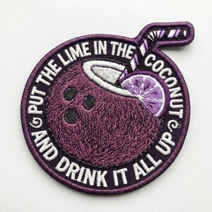 May include: A circular embroidered patch featuring a purple coconut with three black spots, a white straw, and a purple lime slice. The border contains the white text: PUT THE LIME IN THE COCONUT AND DRINK IT ALL UP, set against a dark purple background.