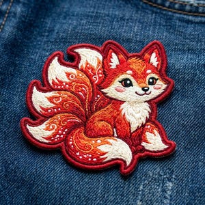 May include: An embroidered patch featuring a stylized nine-tailed fox with vibrant orange and white thread detailing. The fox has large dark eyes, pink cheeks, and intricate swirling patterns stitched into its multiple bushy tails.